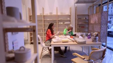 İki kadın seramik atölyede seramik parçalar ve aletlerle çevrili bir seramik atölyede yaratıcı bir süreçle meşgul olan bir çömlek projesini tartışıyorlar.