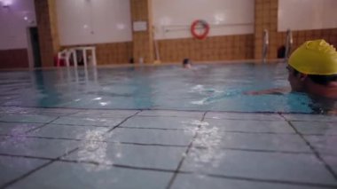 Yüzme şapkası takan yaşlı bir adam ve kadın kapalı bir havuzda yüzerek emeklilikte sağlıklı ve aktif bir yaşam tarzını gösteriyor.