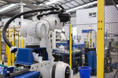 Modern robotik kol modern bir fabrikanın içindeki üretim bandında malzeme topluyor, otomasyon ve gelişmiş üretim süreçlerini gösteriyor.