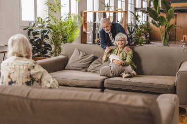 Üç kıdemli arkadaş rahat bir oturma odasında gevşeyip sohbet ediyorlar. Birbirinin arkadaşlığından zevk alıyorlar ve kahkahalarını paylaşıyorlar. Sıcak bir bağ ve mutluluk ortamı yaratıyorlar.