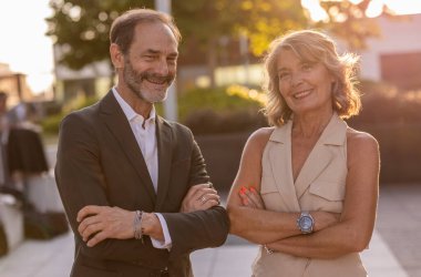 İki mutlu iş adamı, kollarını kavuşturup şehrin dışında dikilirken, gün batımının sıcacık parıltısının ve güven ve başarının tadını çıkarıyorlar.