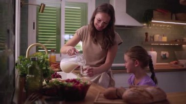 Sıcak bir mutfak ortamında mutlu aile anları, bir anne kızı için sevgiyle süt döker, iç mutluluğun iç açıcı bir sahnesini yaratır.
