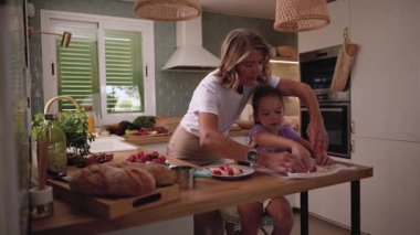 Mutlu büyükannesi torununa modern ve parlak bir mutfakta ekmek ve diğer malzemelerle çilek kesmeyi öğretiyor.