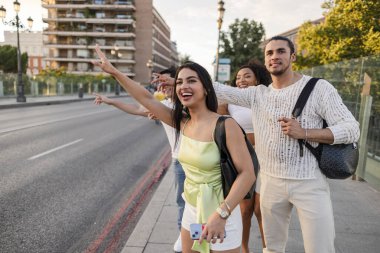 Bir grup genç yetişkin arkadaş coşkuyla el kaldırıyor ve şehrin kaldırımlarında durup, şehir ulaşımı için taksi çağırıyorlar.