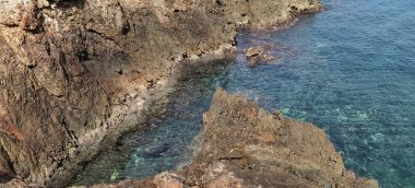 Dalgalar engebeli bir sahil şeridinde yükselen kayalara çarparlar, doğanın gücünün ham sahil güzelliğiyle buluştuğu yerde.