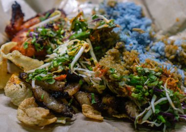 Mavi pilav, ızgara tavuk, ızgara et, şifalı ot, kraker ve meze ile dolu renkli bir Nasi Kerabu servisi..