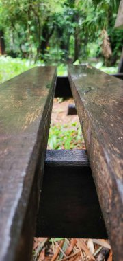 Yeşillik yeşil bir park ortamındaki ahşap bankın yakın perspektifi, ormanın kırsal ve doğal hissini vurgulayan eskimiş dokuya ve sıcak tonlara odaklanıyor..