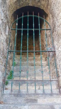 Zirveye çıkan tarihi bir taş merdiven, yıpranmış demir bir kapıyla çevrili, taş basamaklarda çalılıklar, gizemli ve antik bir mimariyi çağrıştırıyor..