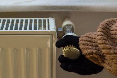 Hand in gloves and thick winter sweater controls the natural gas valve.