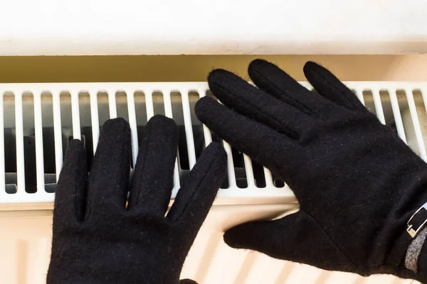 Black gloved hand warming up on the radiator