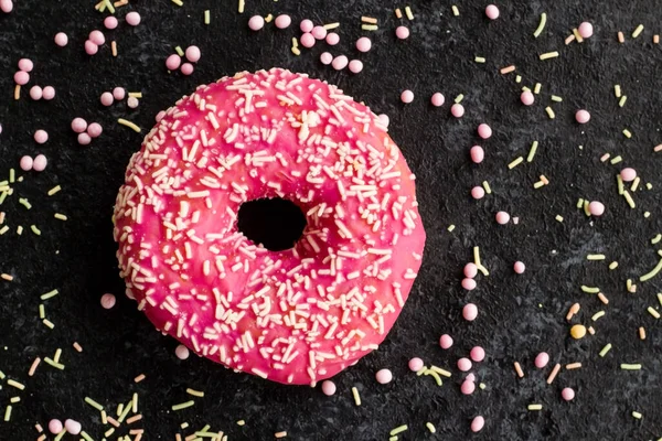 Pink colored, sweet donuts are designed with decoration candies on a black surface.