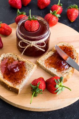 Doğal çilek reçeli, iki dilim ekmek ve yuvarlak tahtada bir bıçak.