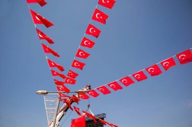 Mavi gökyüzünde rüzgarda dalgalanan bir sokak lambasına bağlı üç sıra Türk Bayrağı