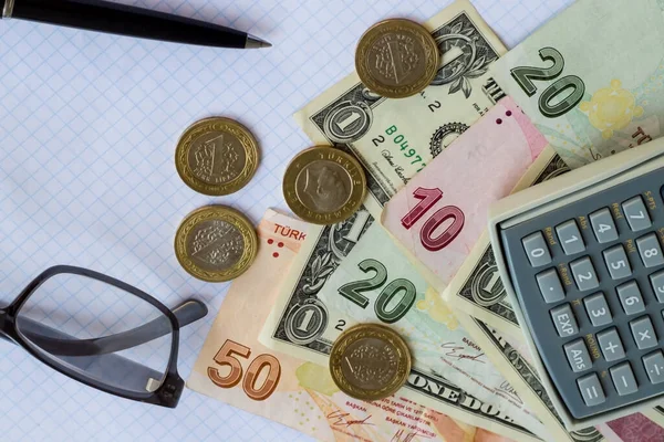用钢笔 智能手机 硬币和计算器在检查过的白纸上印上土耳其钞票和美元 — 图库照片