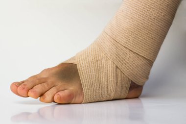 Tıbbi bandaj, kadın burkulmuş sol ayak bileğine dolamış. Beyaz arka planda, yansıma ve kopyalama alanı var.