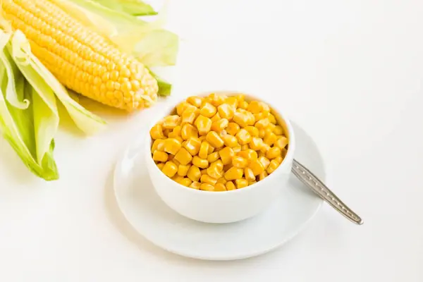 Boiled, fresh sweet corn in bowl with natural corn cob on white surface