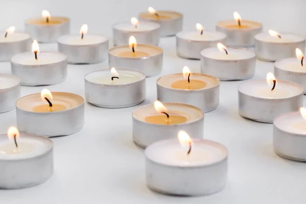 Many small round candles,tealight burns on a white background,conceptual image