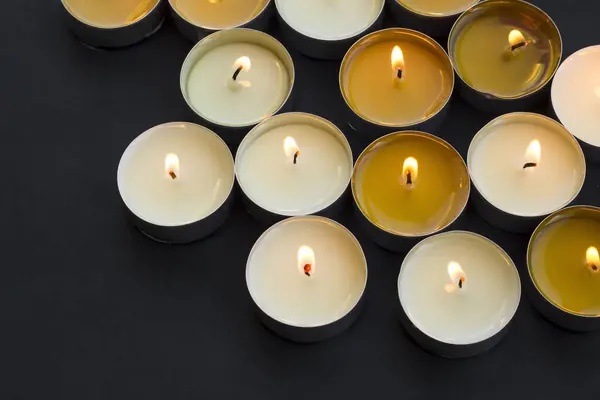 Many small round candles,tealight burns on a black background with copy space,above view
