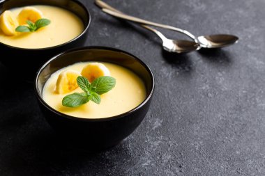 Siyah yüzey üzerinde siyah kasede muzlu pudingin yakın çekimi.