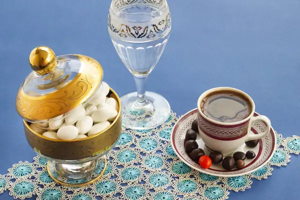 伝統的なトルコのハード コーヒー 水および手作りのレースの布が付いている青い表面で設計されているアーモンドのキャンディ ラマダンの後の砂糖の饗宴 ロイヤリティフリーのストック画像
