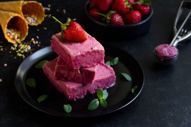 Çilekli dondurma, siyah yuvarlak bir tabakta tasarlanmış, taze çilekli.