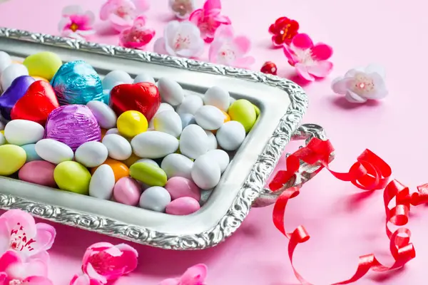Renkli Badem Şekeri Gümüş Çikolata Tepsisi Pembe Yüzeyde Bahar Çiçekleriyle - Stok İmaj