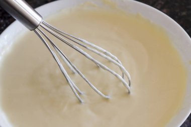 Beyaz bir kasede, süt, yumurta ve un çırpın. Pişirmeden önce hazırlık