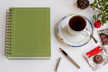 Hard cover annual agenda on the white surface with stylo pen,a cup of tea  clipart