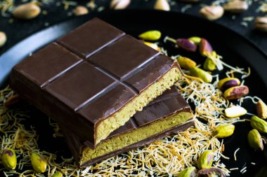 Dilimlenmiş Dubai Çikolatası, şam fıstığı ve kunefe parçalarıyla siyah bir tabakta.