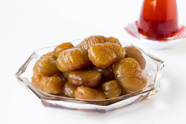 Geleneksel Türk Şekerleme Kestaneleri beyaz yüzeyde çay ile cam tabakta dizayn edildi