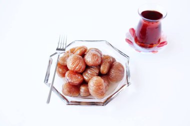 Geleneksel Türk Şekerleme Kestaneleri beyaz yüzeyde çay ile cam tabakta dizayn edildi