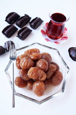 Geleneksel Türk Şekerleme Kestaneleri beyaz yüzeyde çay ile cam tabakta dizayn edildi
