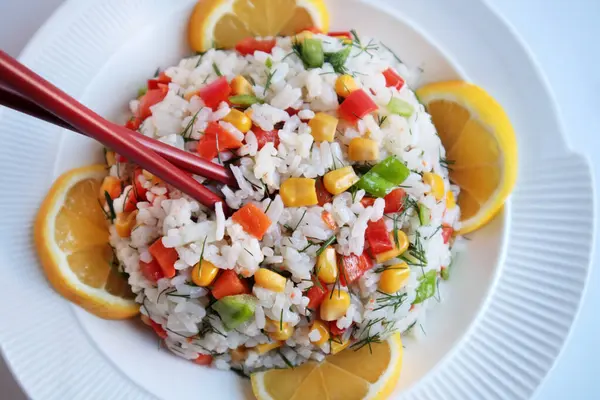 Pirinç salatası veya Asya mutfağından renkli sebzelerle dilimlenmiş limon ve çubuklarla servis edilen pilav.