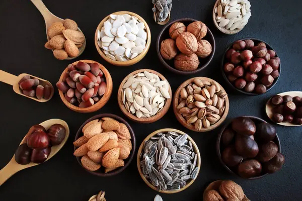New harvest nuts in shells, designed on a black background in wooden bowls.Large nuts group