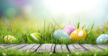 Altı boyalı Paskalya yumurtası bir bahar gününde yeşil çimen çayırı, parlak güneş ışığı ve fotokopi alanı olan sıcak bir arka plan ve ürünleri sergilemek için ahşap bir bank ile mutlu bir Paskalya kutlaması..