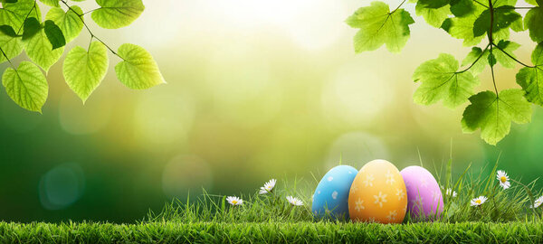 Три раскрашенных пасхальных яйца, празднующих счастливую Пасху в весенний день с зеленым лугом травы, ярким солнечным светом, листьями деревьев и теплым цветовым фоном с копировальным пространством.