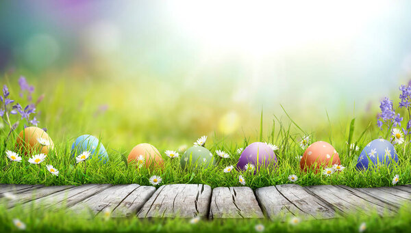Seven painted easter eggs celebrating a Happy Easter on a spring day with a green grass meadow, bright sunlight and a warm colour background with copy space and a wooden bench to display products.