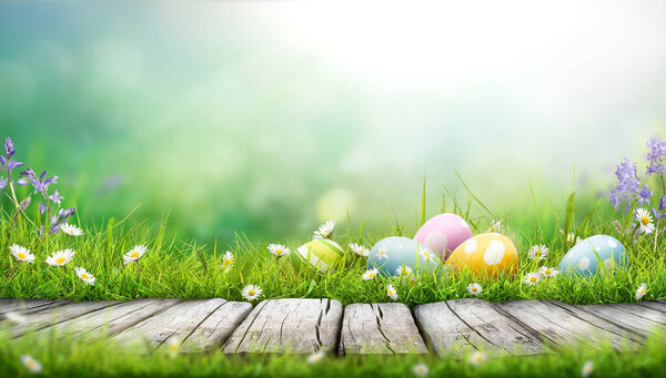 Five painted easter eggs celebrating a Happy Easter on a spring day with a green grass meadow, bright sunlight and a cool colour background with copy space and a wooden bench to display products.