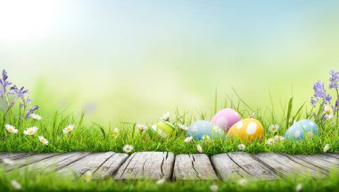 Beş tane boyanmış Paskalya yumurtası bir bahar gününde yeşil çimen çayırı, parlak güneş ışığı ve fotokopi alanı olan sıcak bir arka plan ve ürünleri sergilemek için ahşap bir bank ile mutlu bir Paskalya kutlaması..