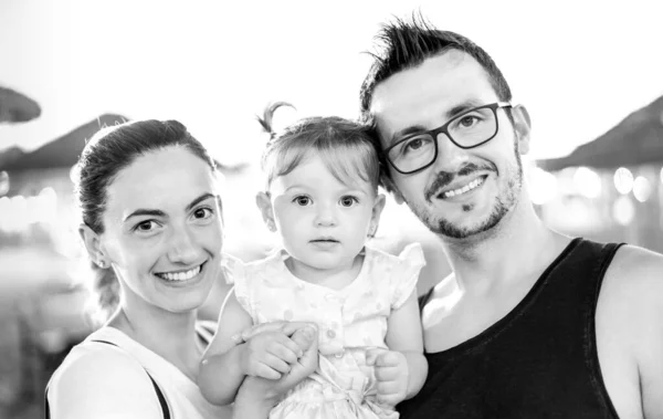 Family picture of smiling young mom and dad posing in beach with cute little daughter - Summer party