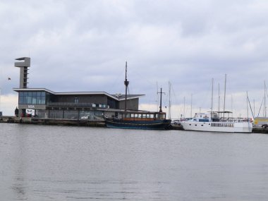 Rıhtım sahnesinde bulutlu bir gökyüzü altında liman, tekne ve mimari