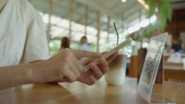 Kadın, kafeteryada nakit olmadan dijital ödeme yapmak için akıllı telefon kullanarak QR kodunu tarıyor. Menüyü ve siparişi seçin ve indirimi toplayın. Cüzdan, teknoloji, online ödeme, kredi kartı, banka uygulaması, tarama