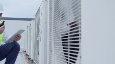 Asyalı bakım mühendisi, fabrikanın çatısındaki işi açıklamak için telsiz kullanıyor. Müteahhit kompresör sistemini denetleyecek ve modern binaların inşaat sahasına hava durumu sistemleri kurmayı planlıyor.