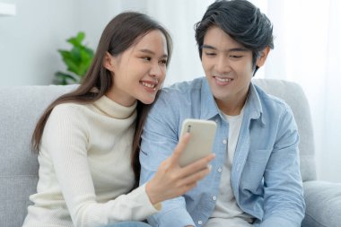 Gülümseyen Asyalı çift internet alışverişinde akıllı telefon kullanıyor. Koca, güzel bir eş için doğum günü hediyesi ödemeye hazır. Balayı için internetten konaklama, uygulama, uçak biletleri..