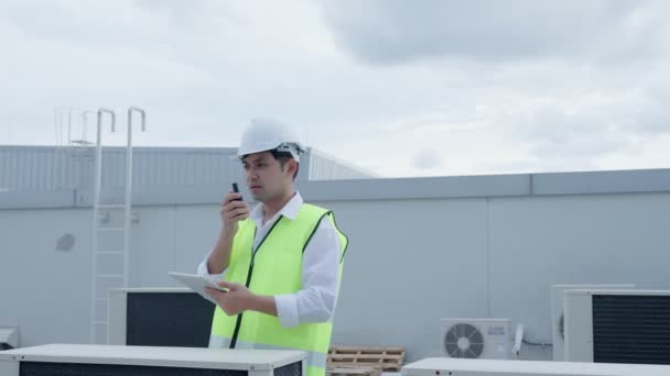 アジアのメンテナンスエンジニアは工場の屋根の上の作品を説明するウォークトークを使用します 請負業者は 圧縮機システムを検査し 近代的な建物の建設現場に空調システムを設置する計画 — ストック動画