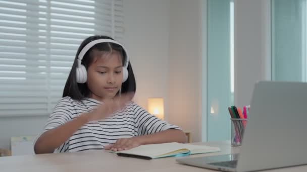 亚洲儿童在线辅导课程 在家里的笔记本电脑上的视频会议 回放在线课程 女生戴耳机学习 笔记作业 视频课程 新教育 — 图库视频影像