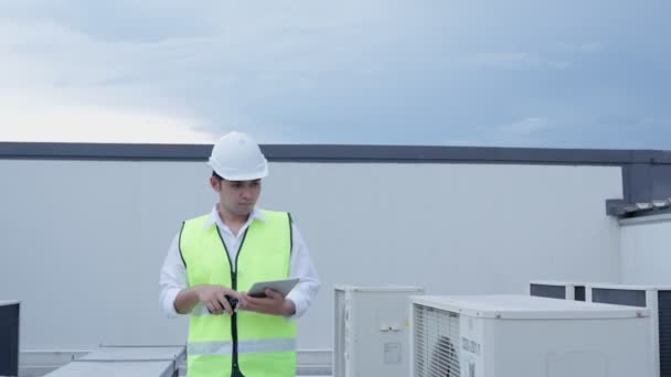 アジアのメンテナンスエンジニアタブレットの再チェック工場の屋根の上で動作します 請負業者は 圧縮機システムを検査し 近代的な建物の建設現場に空調システムを設置する計画 — ストック動画