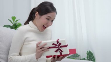 Güzel Asyalı kadın şaşırır ve hediye kutusuyla ilgilenir. Sevimli kız hediye kutusunu açtı. Doğum günü, kutlama, xmas, yeni yıl festivali, teşekkür, kutlama, sevgililer günü, yıldönümü