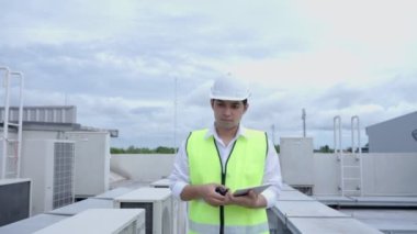 Asian maintenance engineer works on the roof of factory. contractor inspect compressor system and plans installation of air condition systems in construction. technology, online checking, mobile application.