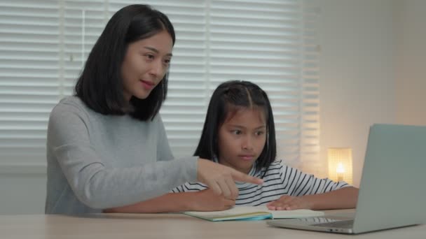 妈妈用笔记本电脑给女儿授课 亚洲小女孩在家里学习 和慈祥的妈妈一起做作业 鼓励她考试 亚洲女孩快乐的家庭学校 妈妈建议一起接受教育 — 图库视频影像